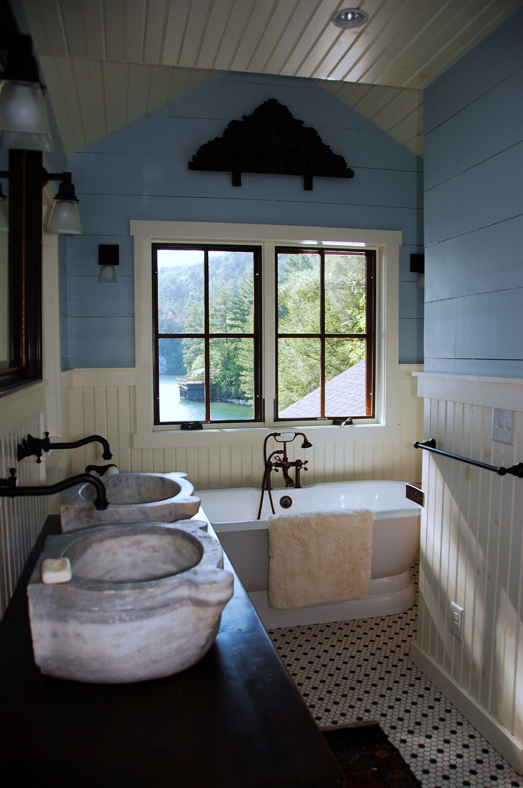 Bathroom with blue walls, white trim, a window overlooking trees, and dual stone sinks.