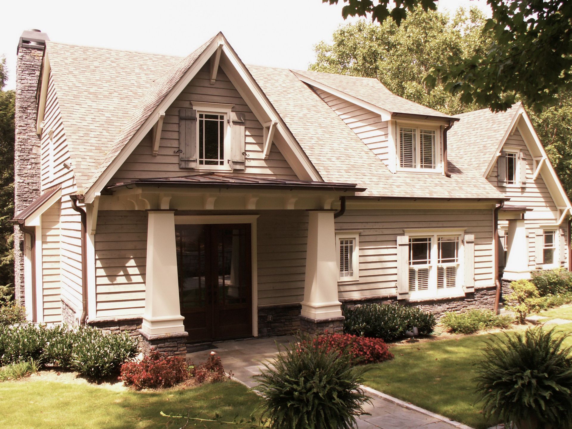 Tan and white craftsman style house with porch, chimney, and landscaping.