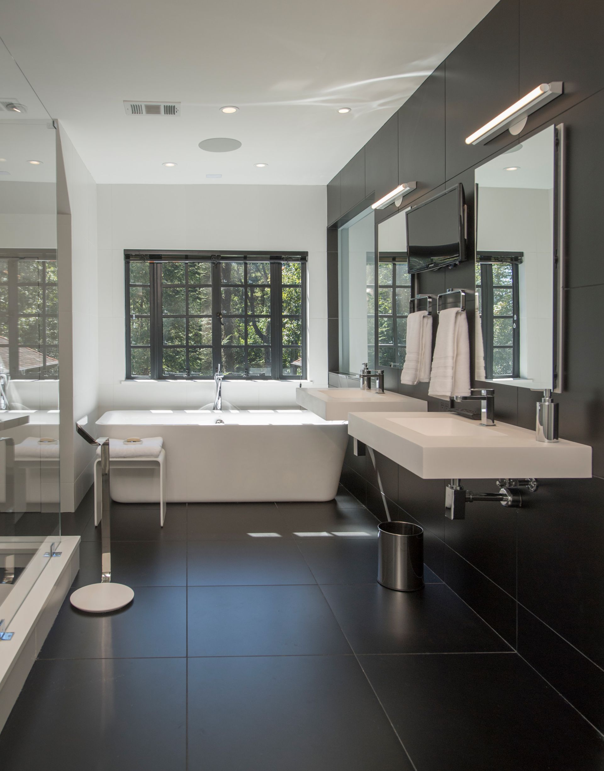 Modern bathroom with black tile floors, white tub, double sink, and large window.