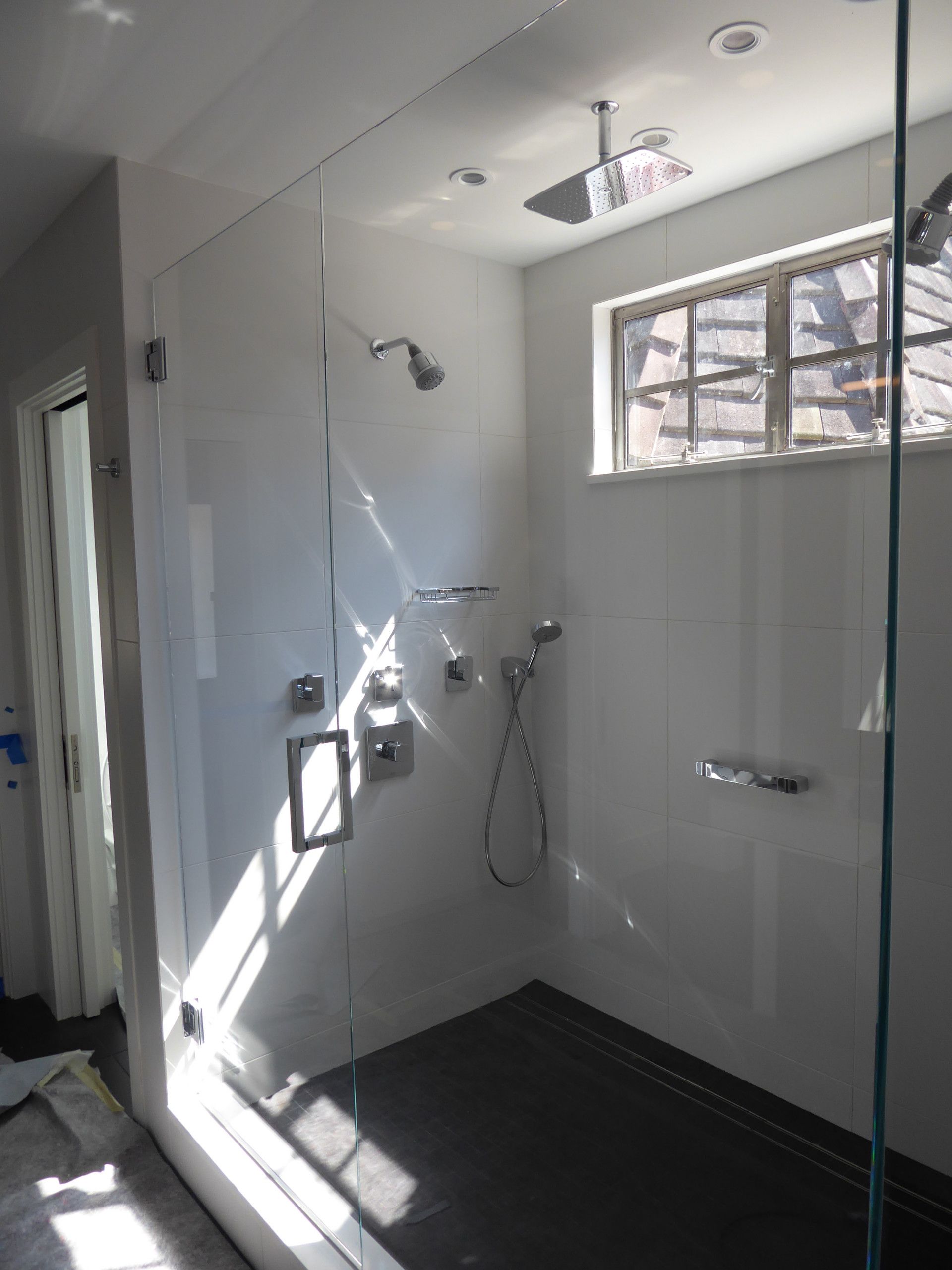 Modern bathroom with glass shower enclosure, white walls, dark tiled floor, window.