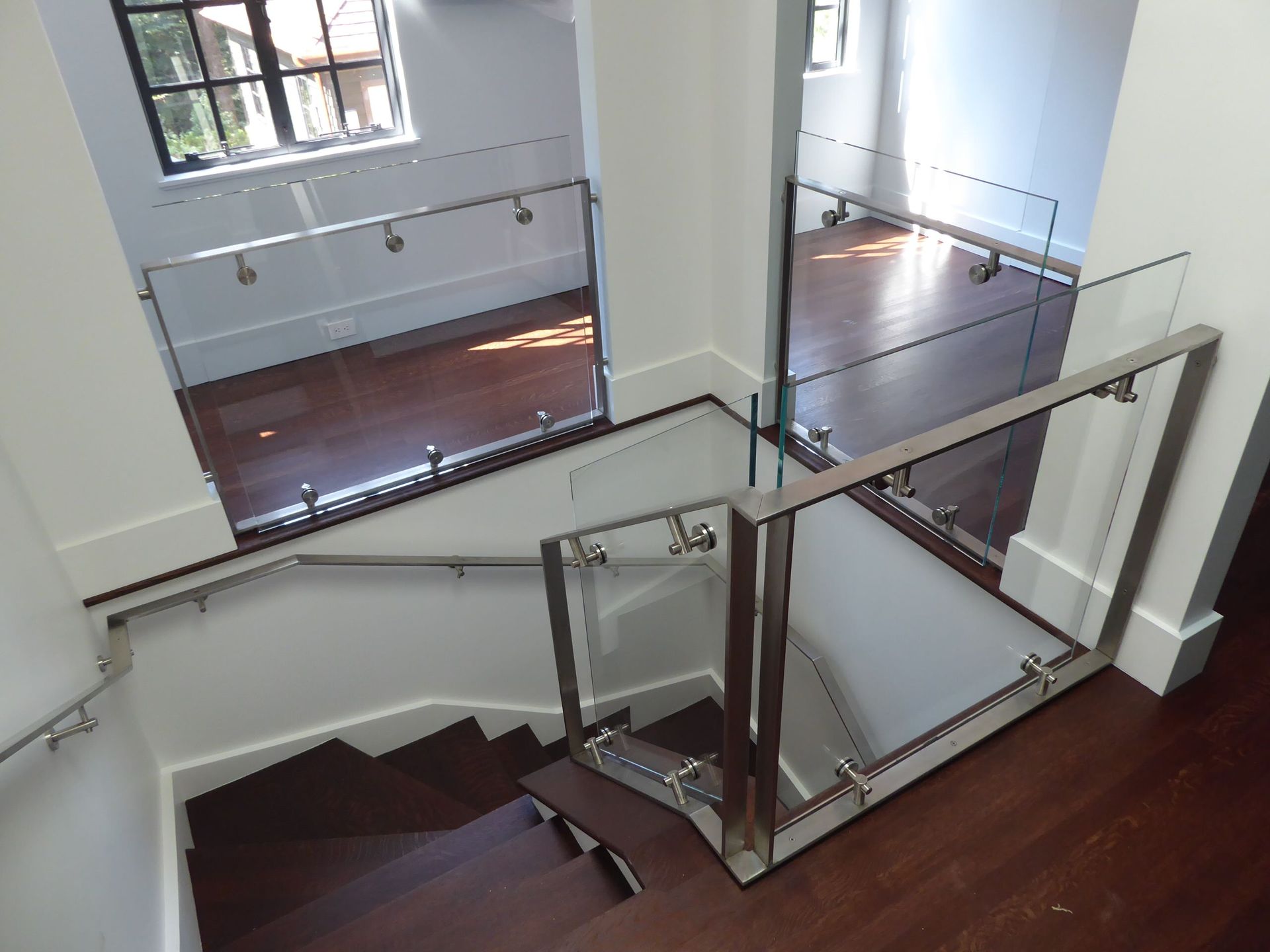 Staircase with glass and metal railings, dark wood steps, and white walls.