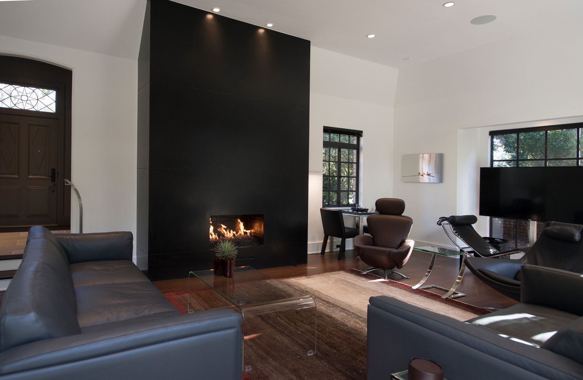 Modern living room with black fireplace, dark furniture, and large windows.