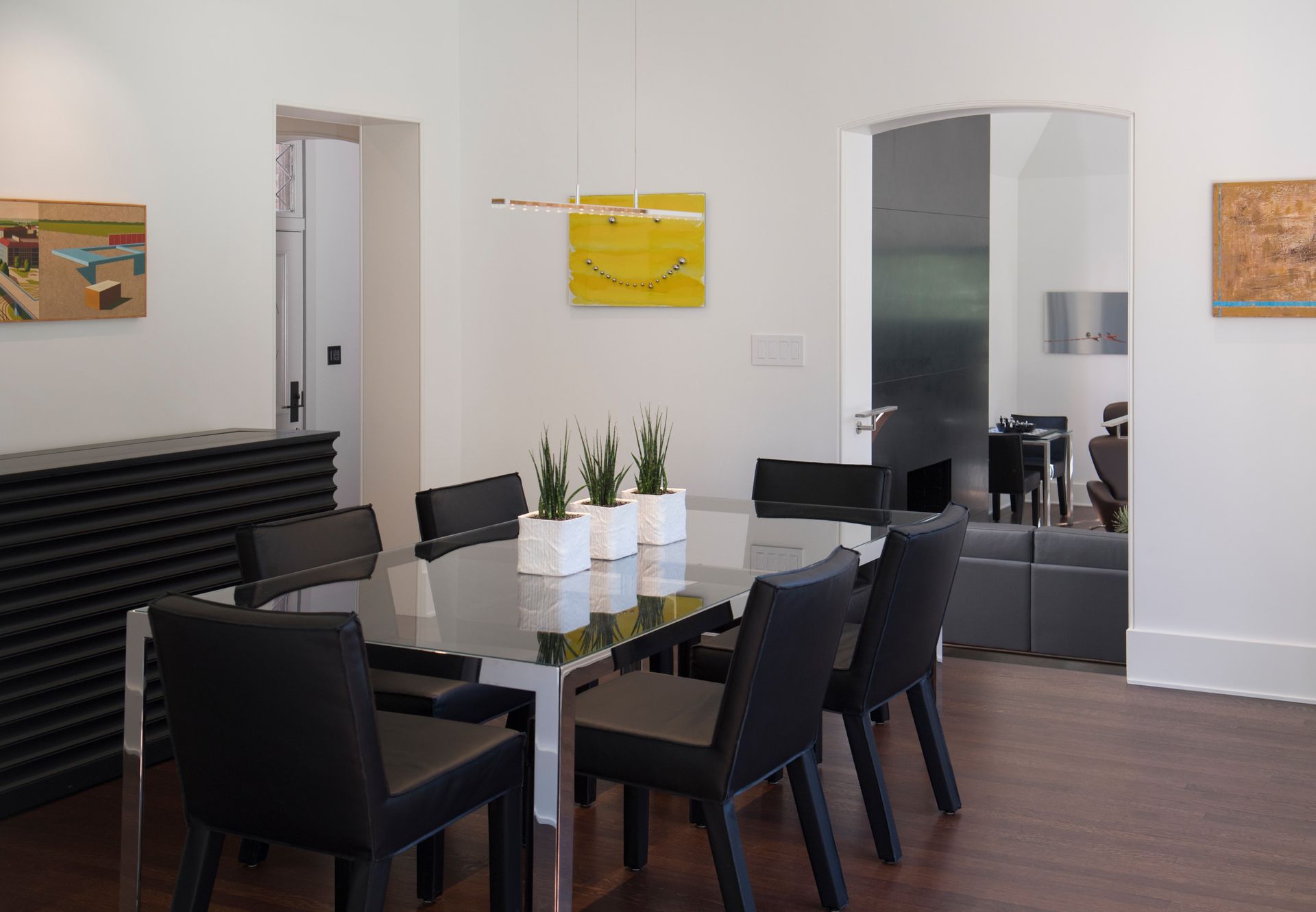 Modern dining room: glass table with black chairs, art on white walls, large mirror.