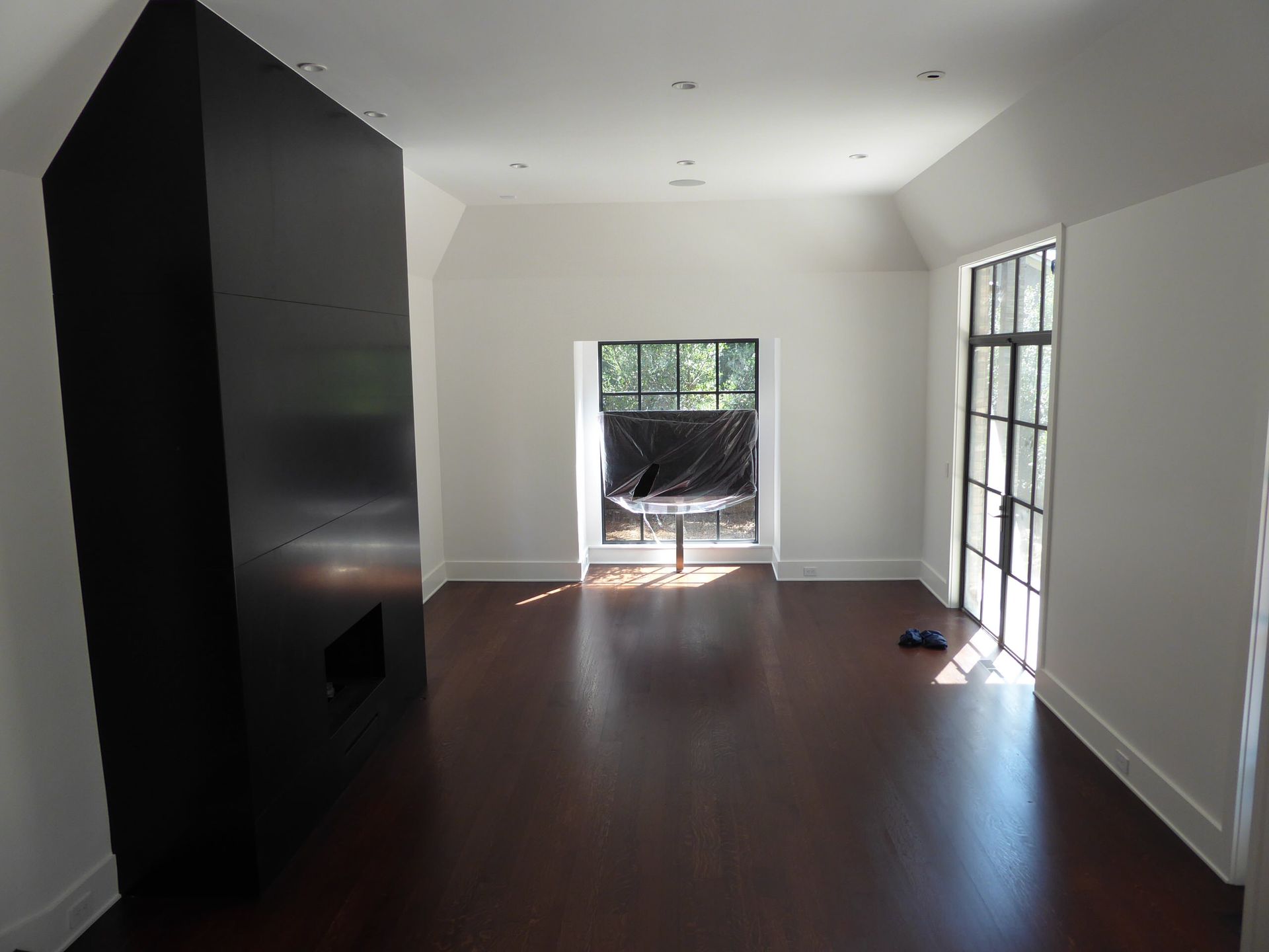 A dark hardwood floor room with a black fireplace, white walls, and a window with a view.