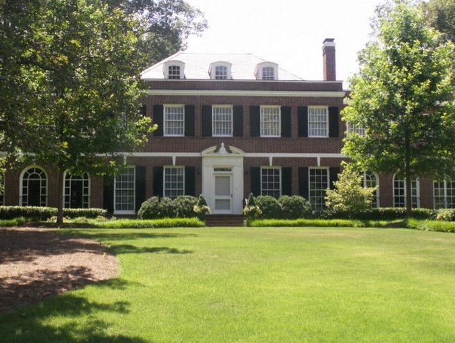 Two-story brick house with white trim, black shutters, and a green lawn.