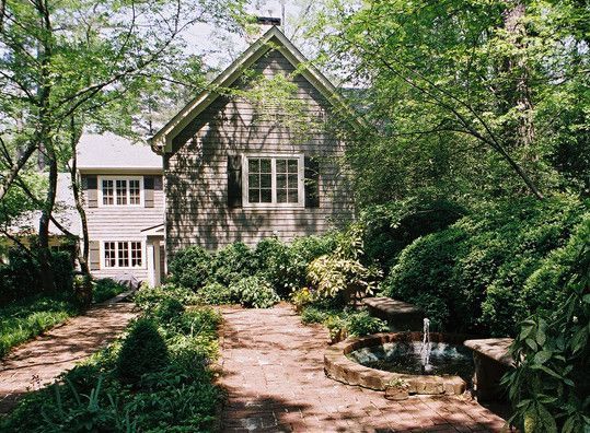 A pathway leads to a weathered wood building with a fountain, surrounded by lush green foliage and trees.