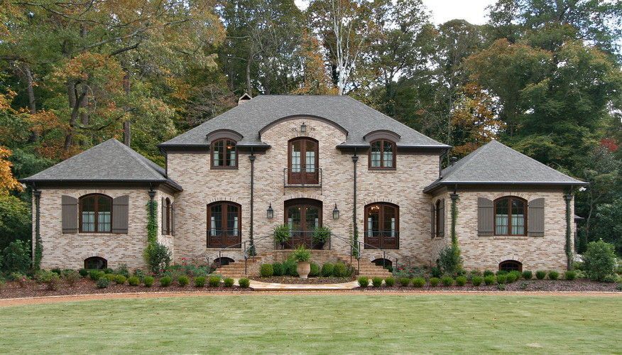 Two-story brick home with dark roof and shutters, surrounded by trees and grass.