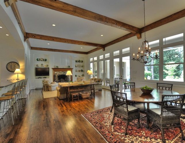 Spacious living/dining room with wood beams, fireplace, and round dining table. Hardwood floors, neutral tones, and large windows.