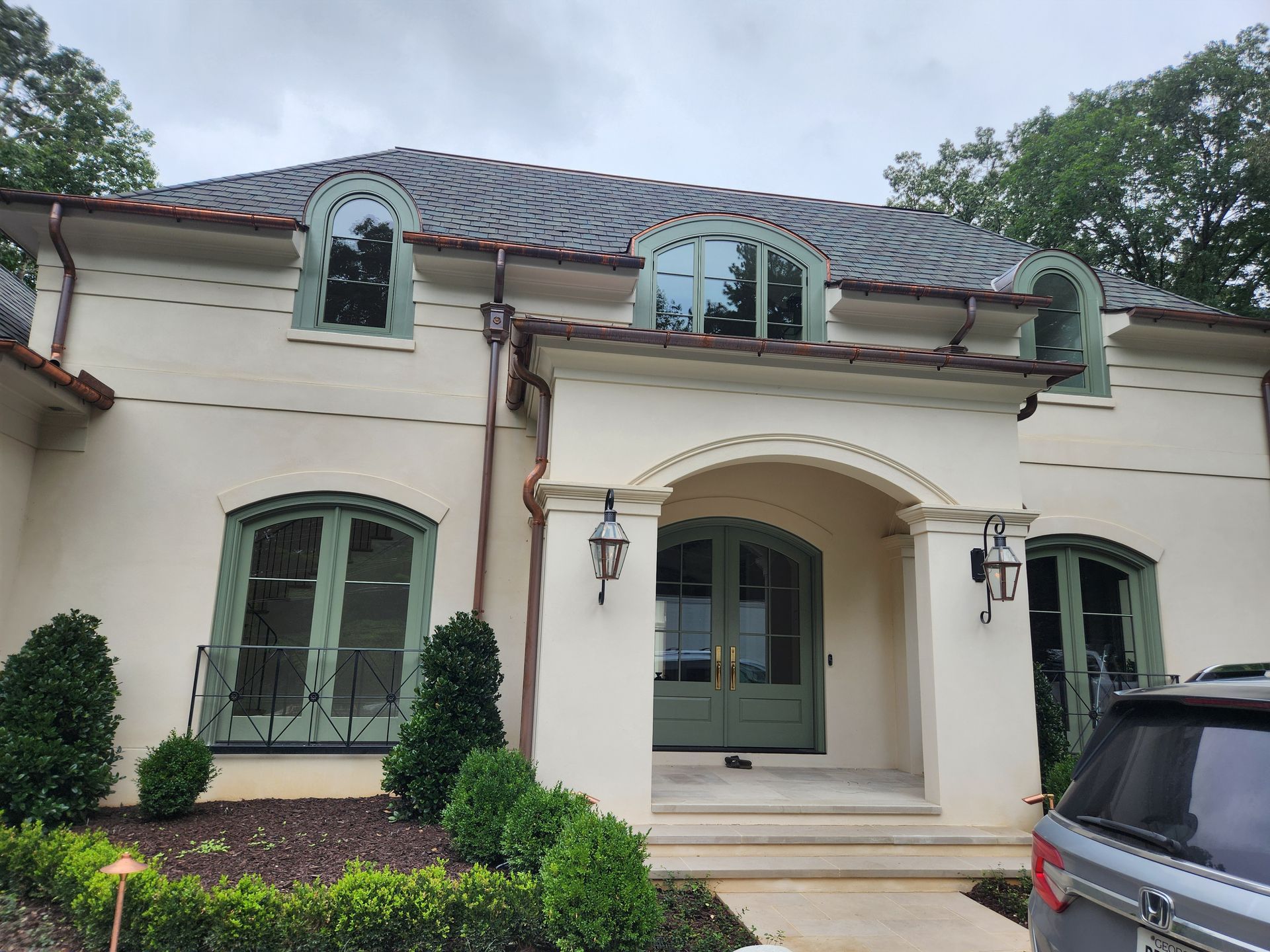 Beige stucco house with green accents, arched windows, and a dark gray tile roof.