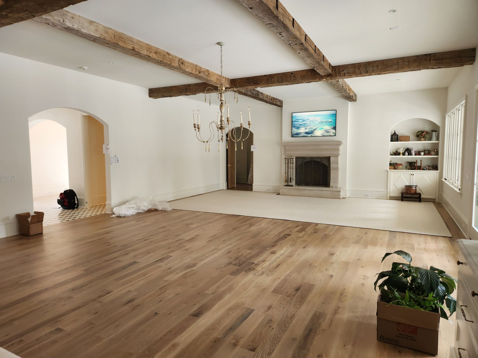 Spacious living room with wood floor, white walls, exposed beams, fireplace, and chandelier.