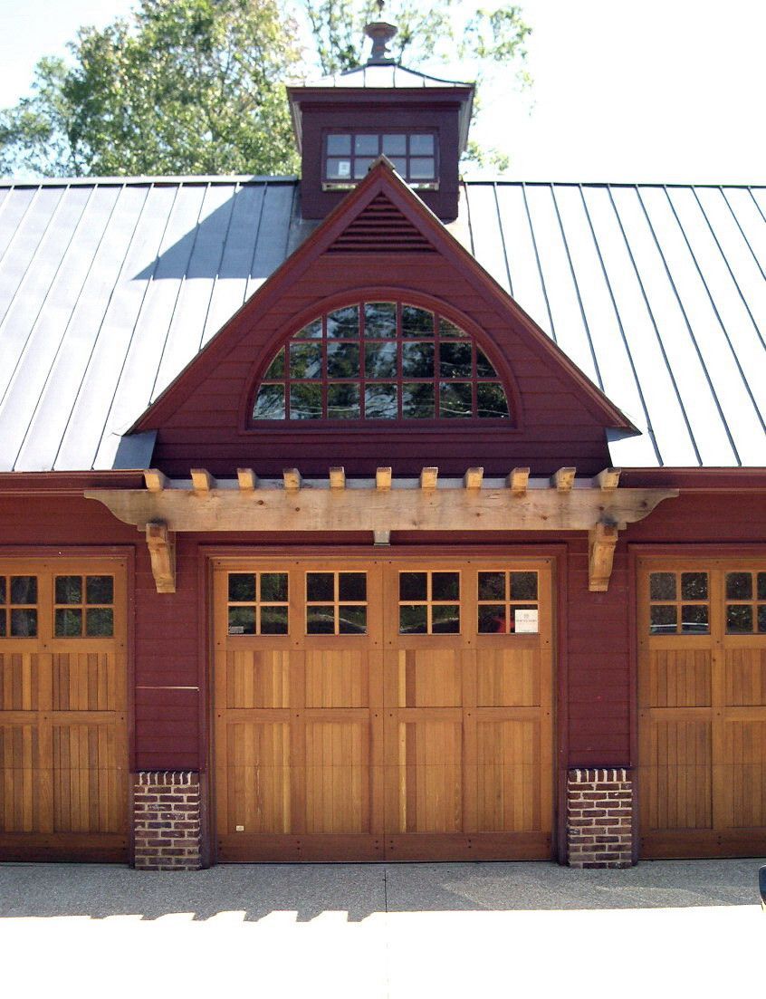 Garage with red trim, wooden doors, and a metal roof. Features a decorative arched window and cupola.