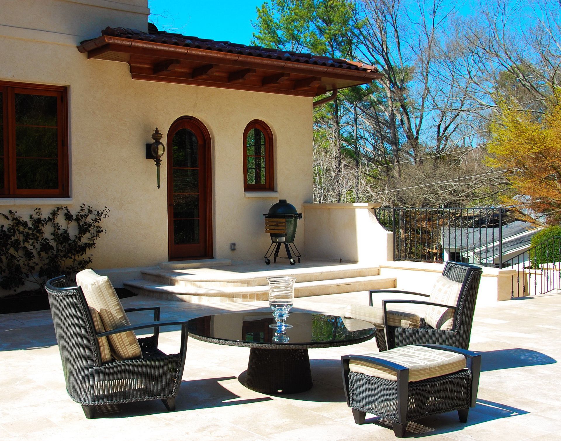 Patio with wicker furniture, stucco building, arched door and windows, grill, sunny day.
