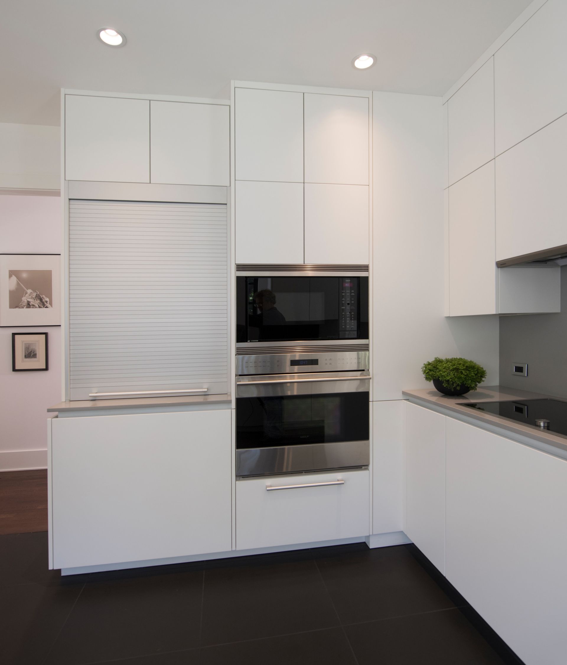 Modern white kitchen with built-in appliances. Microwave, oven, cabinets, and a refrigerator are featured.