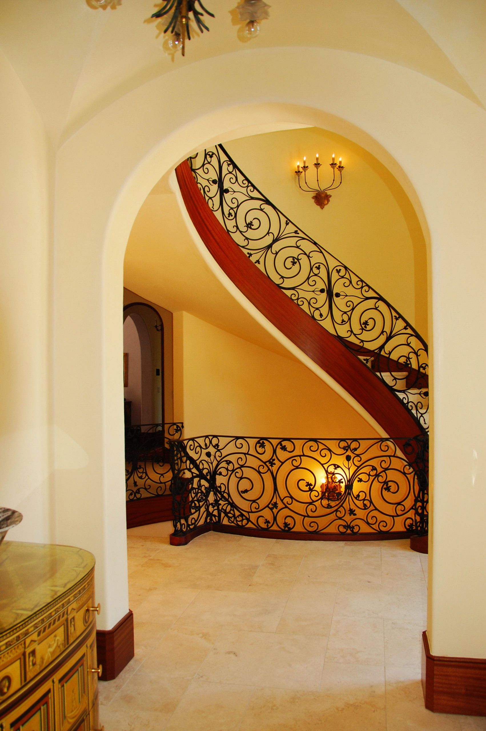 Arched doorway leads to a grand staircase with ornate black railing and wooden banister.