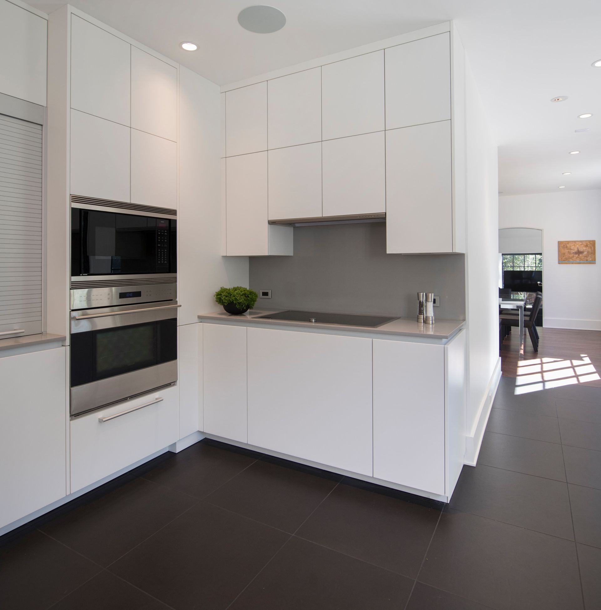 White modern kitchen with dark floor, built-in oven, microwave, and cabinets.