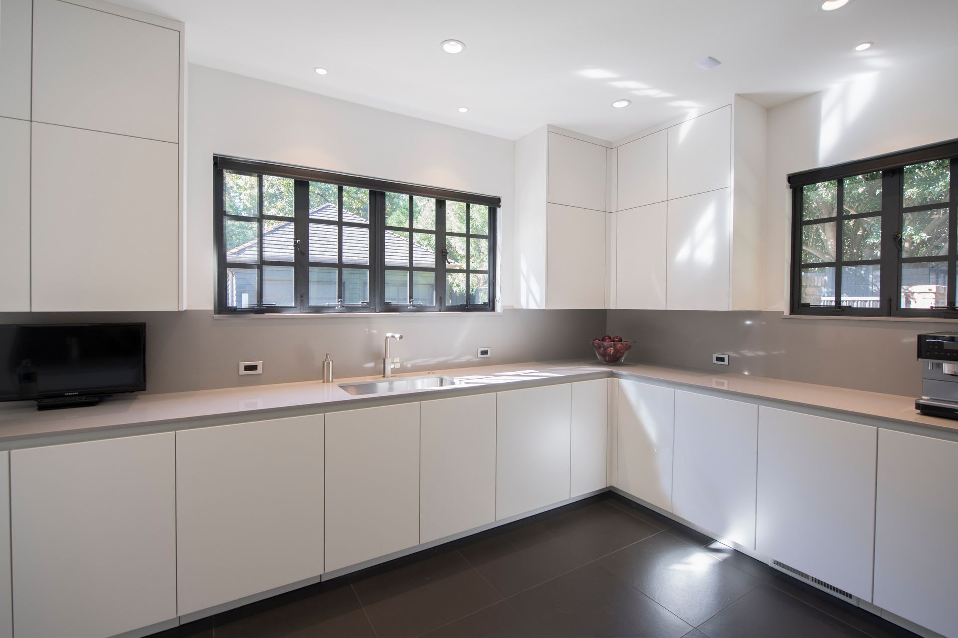 White modern kitchen with gray countertops, dark windows and cabinets, and dark flooring.