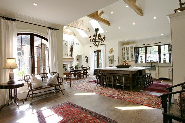 Spacious open-concept kitchen and dining area with arched windows, wooden beams, and antique furniture.