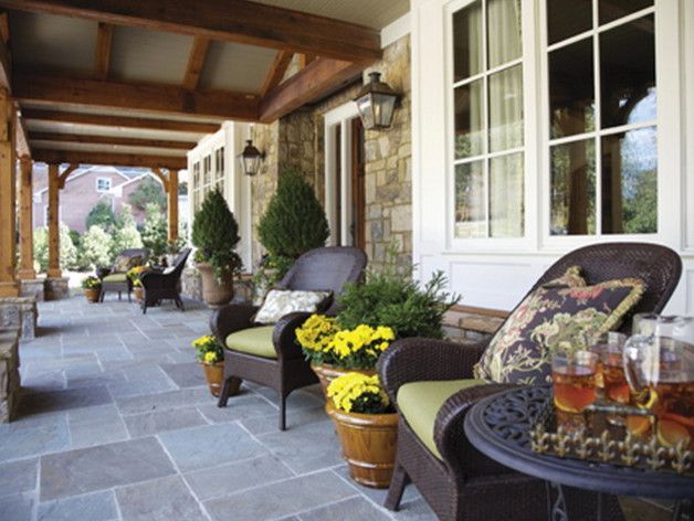 Stone patio with wicker furniture, potted plants, and drinks, under a wooden beam overhang.