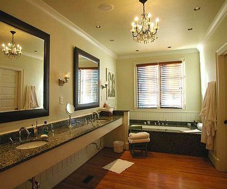 Upscale bathroom with double sinks, dark granite countertop, bathtub, chandelier, and wood floor.