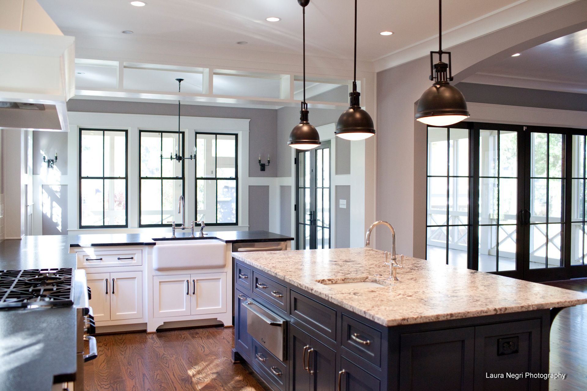 Spacious kitchen with a granite island, white cabinets, dark blue island, and pendant lights.