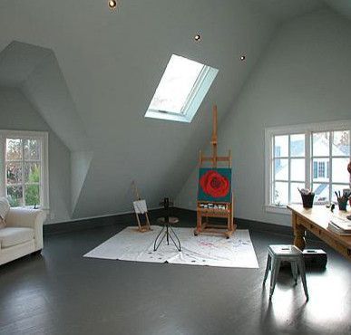 Art studio in an attic with skylight. Easels with art on a grey floor, white walls.