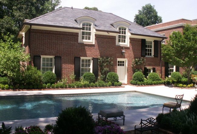 Brick house with pool; dark roof, white trim. Green bushes surround the pool area.