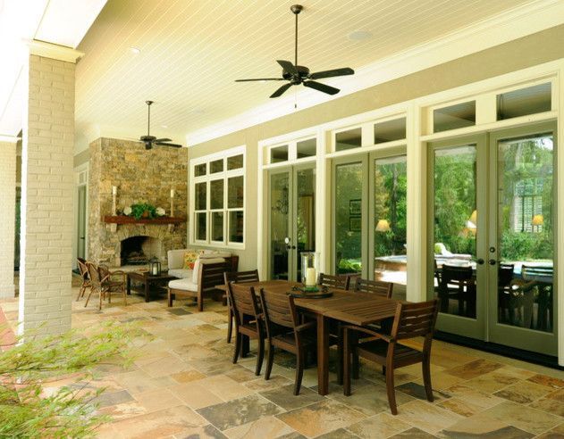 Covered patio with stone fireplace, wooden dining set, and large windows overlooking a garden.