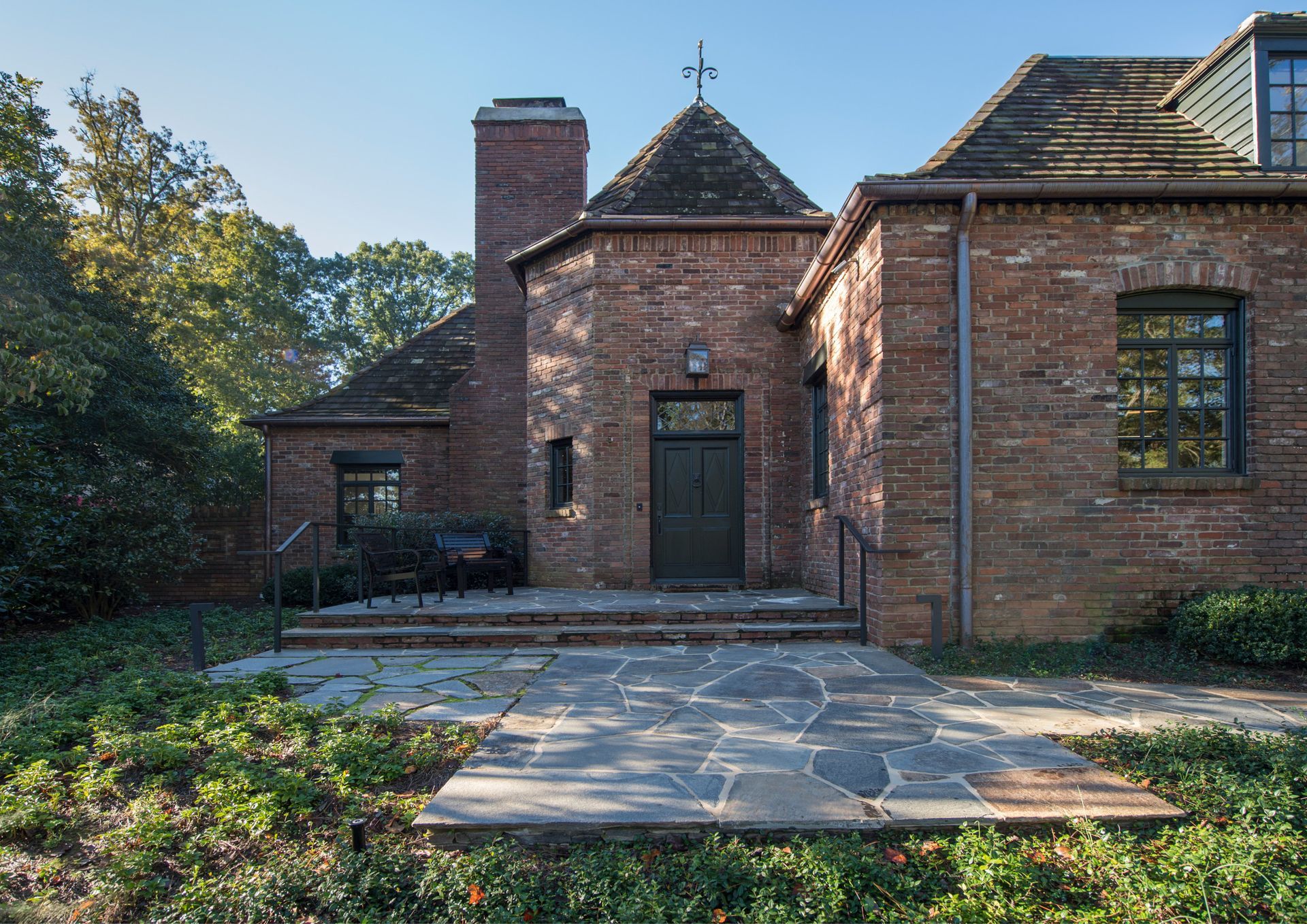 Brick building entrance with stone steps, green door, chimney, and cross on top.