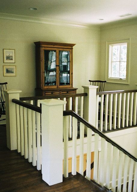 White staircase with wooden railing, cabinet, and window in a light-colored room.
