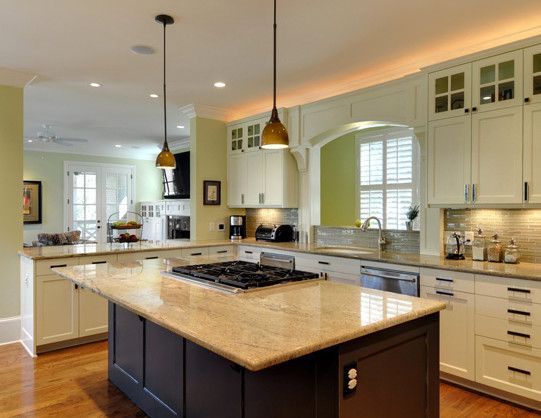 A modern kitchen with a dark island, gas stovetop, light granite counters, and white cabinets.