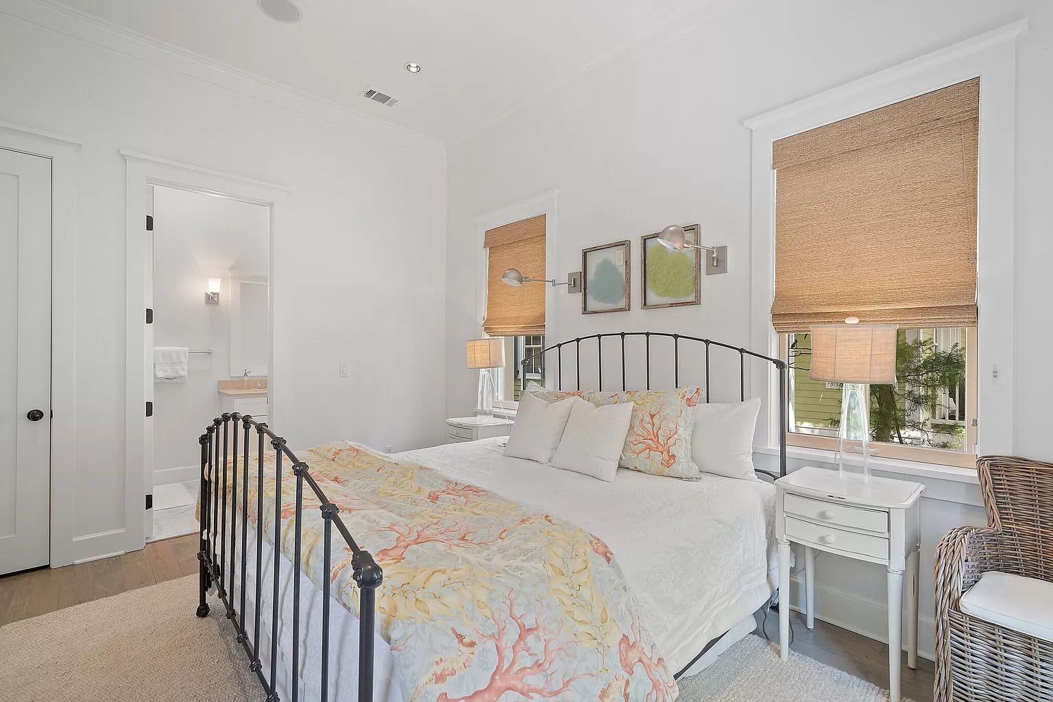 Bedroom with white walls, a wrought-iron bed, and a small bathroom visible. Coastal decor with coral accents.