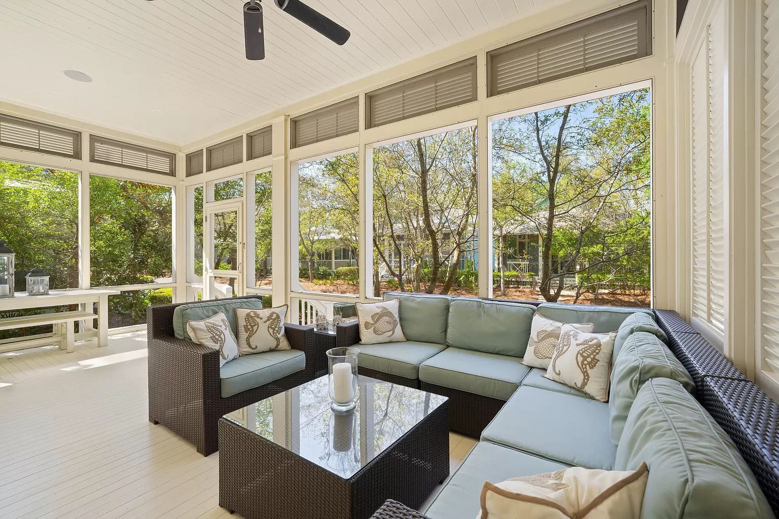 Screened-in porch with blue sectional sofa and wicker furniture; trees visible outside windows.