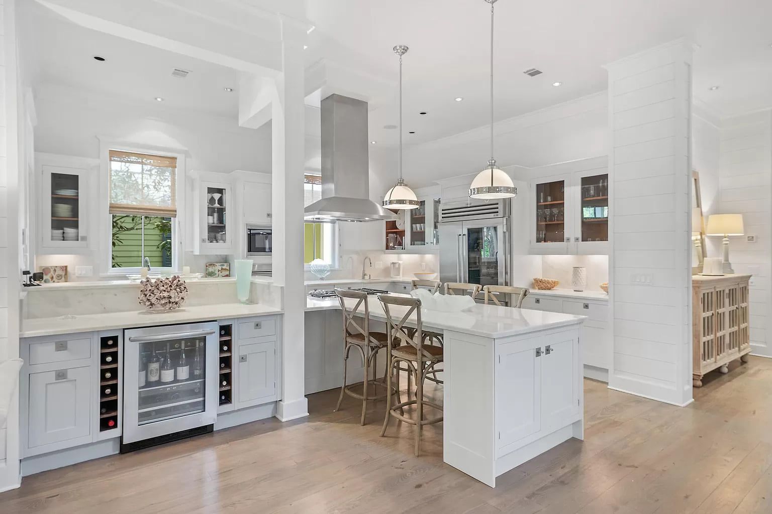 White kitchen with a wine fridge, island with seating, and pendant lights.