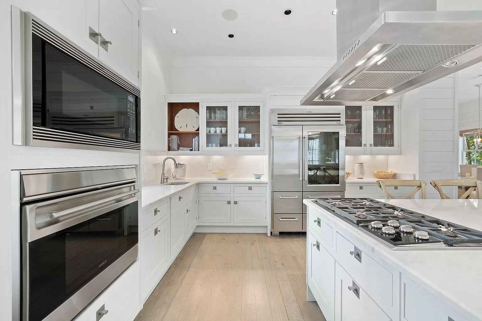 Modern white kitchen with stainless steel appliances, island, and light wood floors.