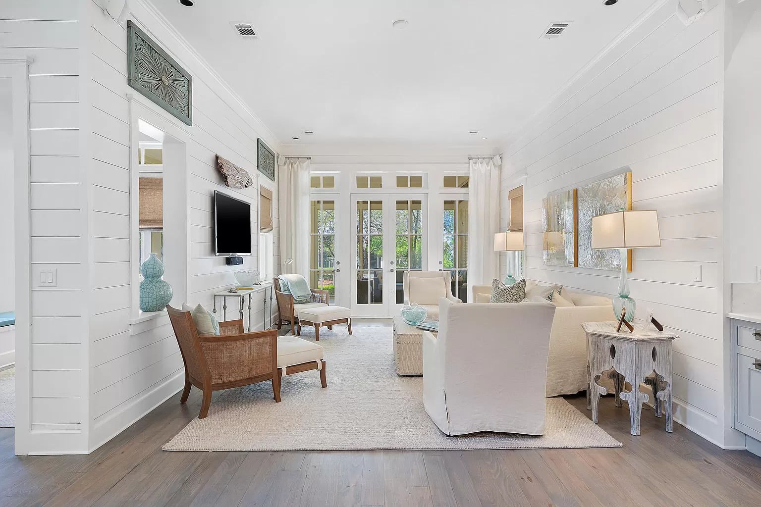 Bright, coastal living room with white walls, hardwood floors, and French doors leading outside.