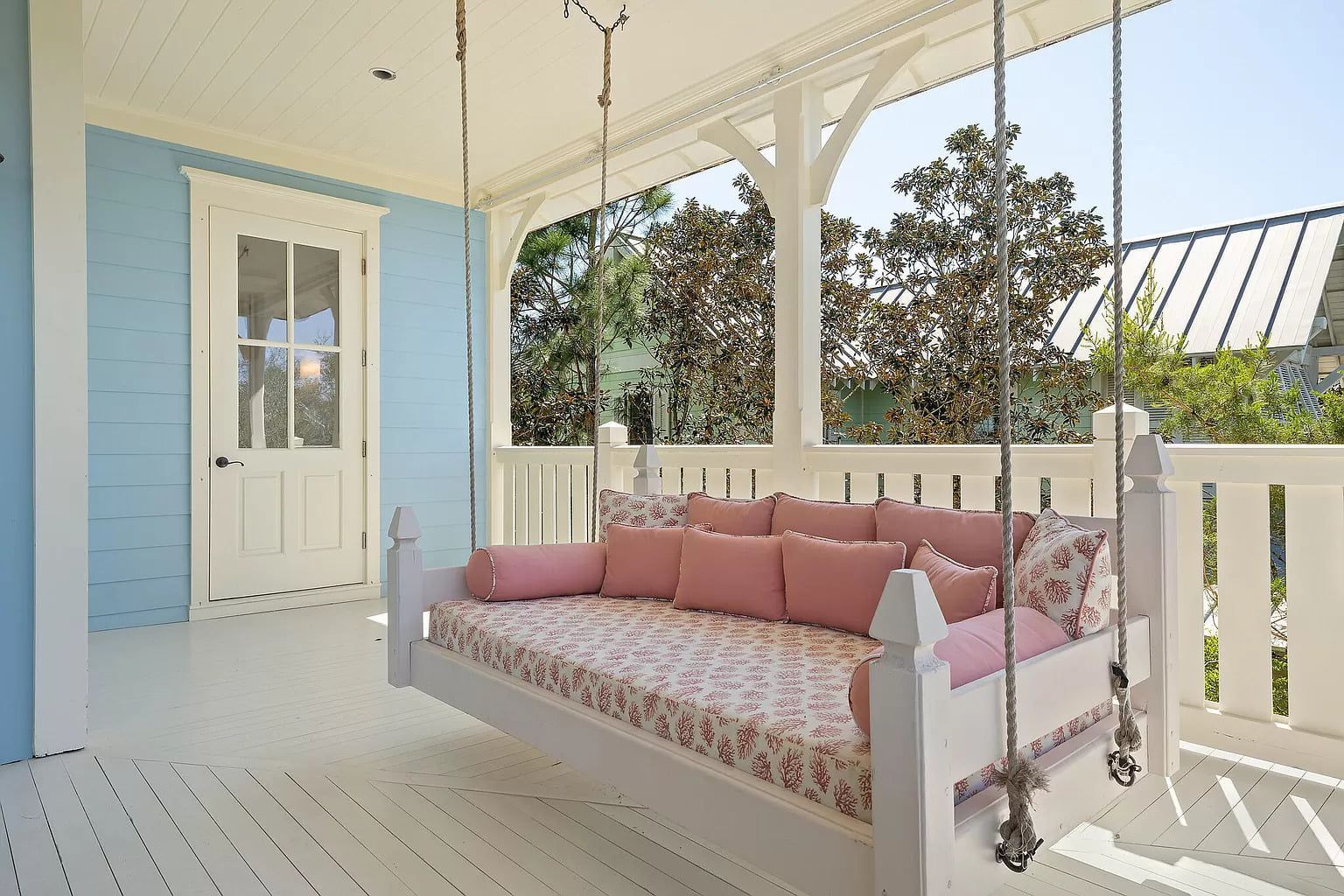 Blue porch with white accents, a swing bed with pink cushions, and a door.