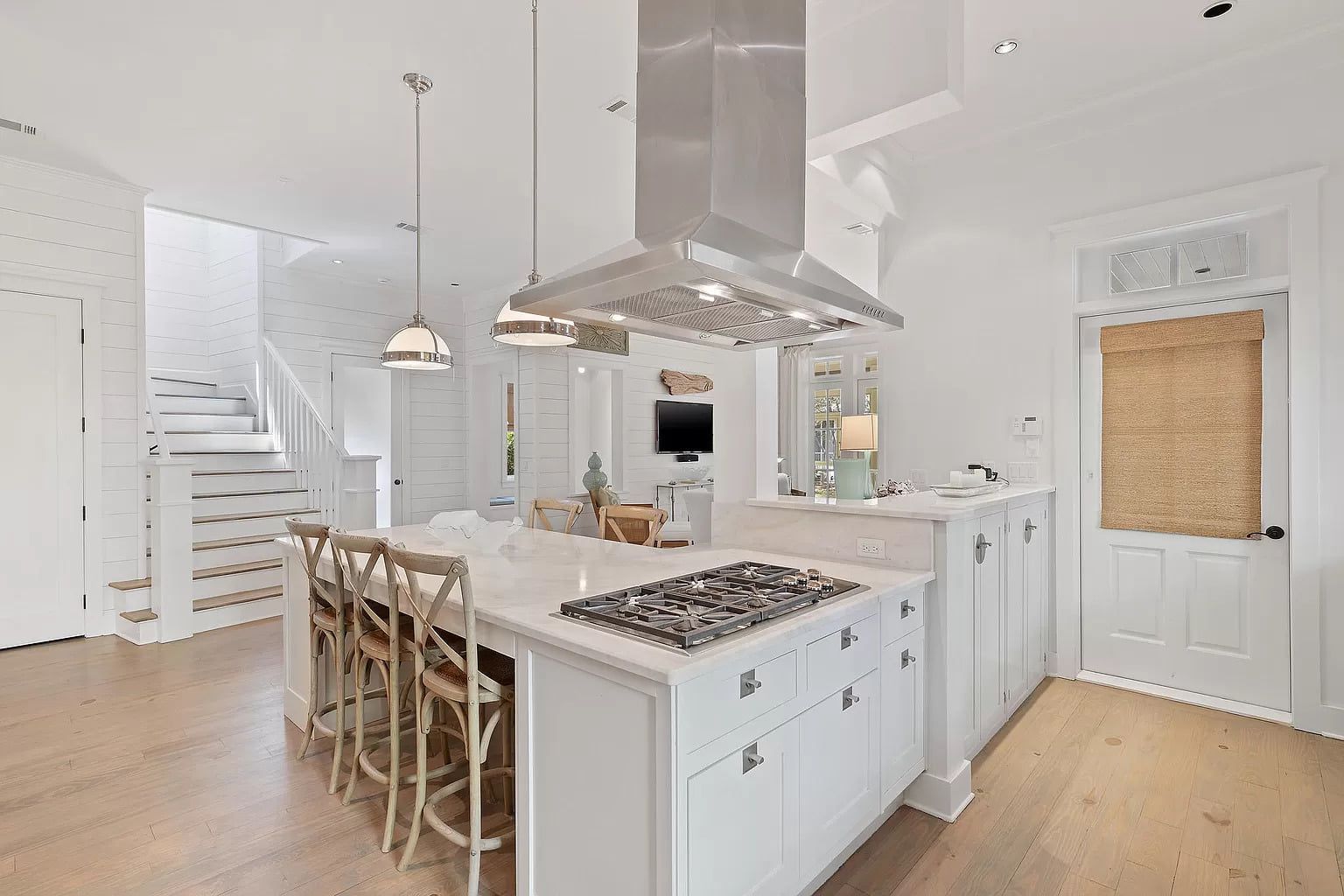 White kitchen with island, gas stove, and bar stools. Staircase and door visible.