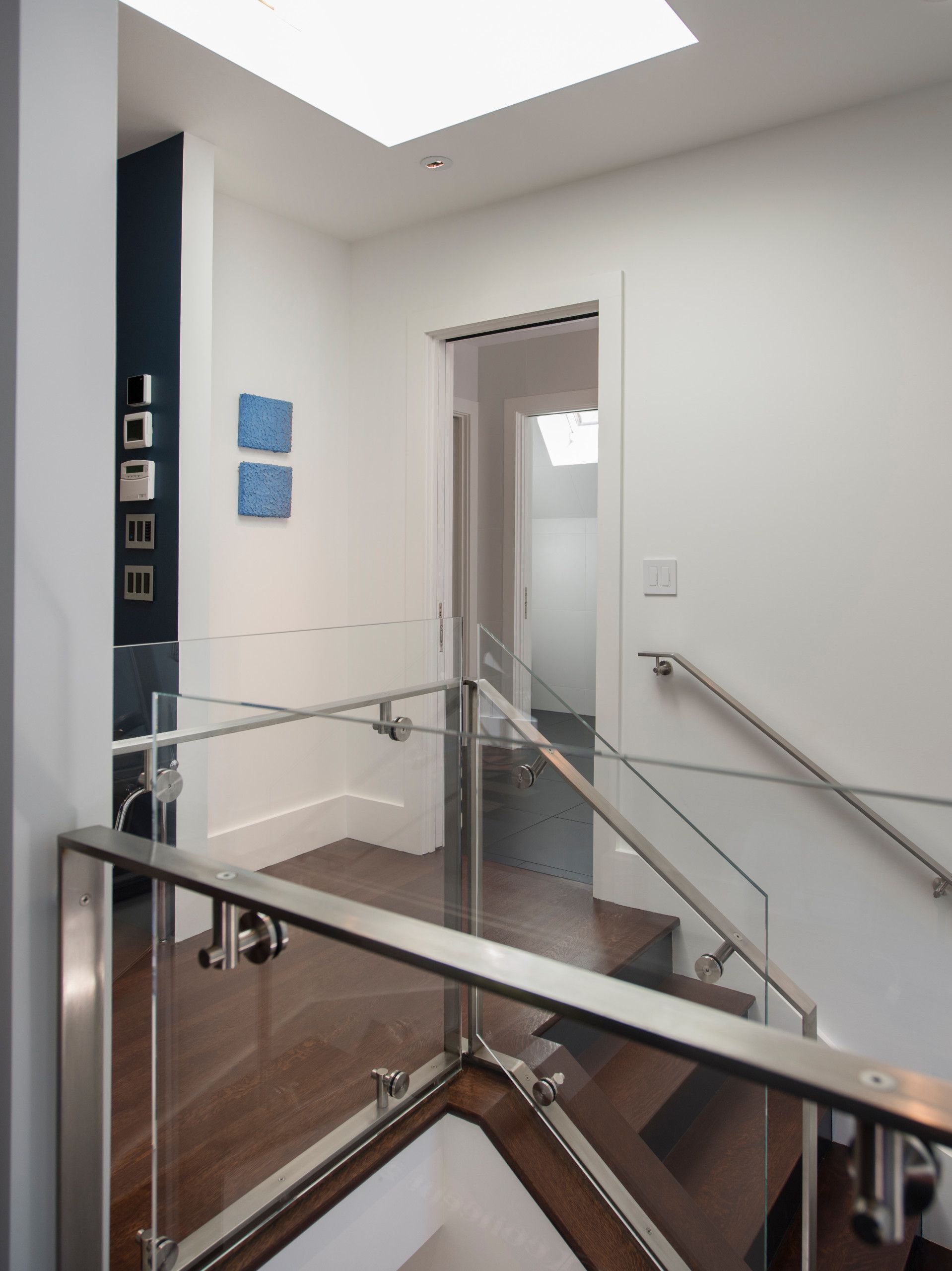 A bright hallway with a glass railing, stairs, and doorway leading to another room.