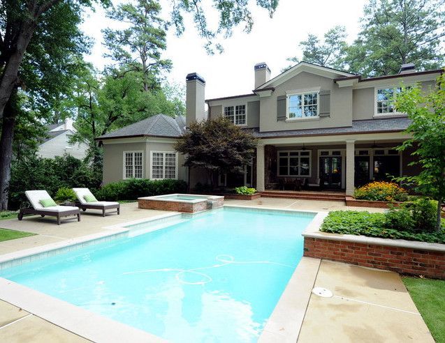 Backyard with pool, spa, lounge chairs, patio, and beige house surrounded by trees.