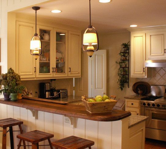 Kitchen with cream-colored cabinets, wooden countertop, and pendant lights. Bar stools are at the counter.