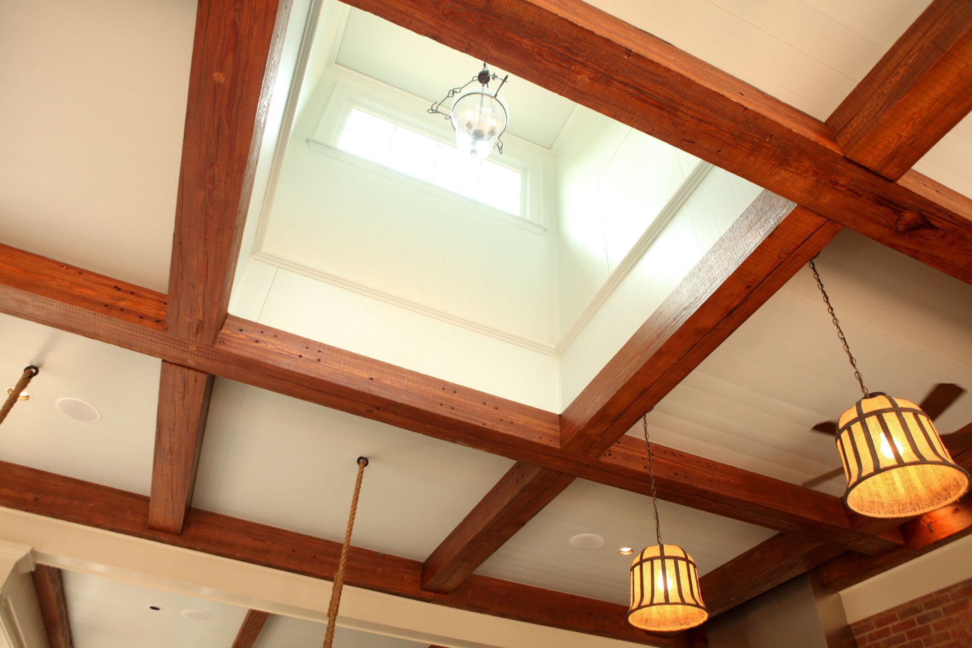Wooden beam ceiling with a skylight, hanging lamps, and white walls.
