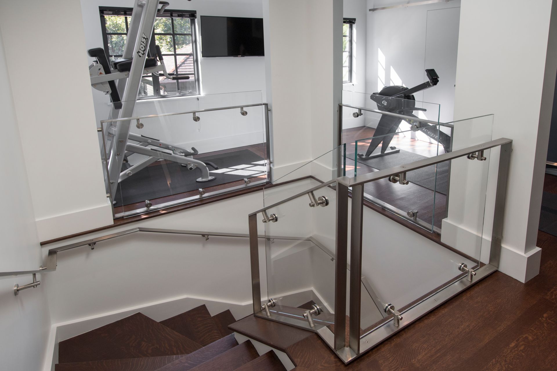 Staircase with a glass and steel railing leading to a gym with exercise equipment.