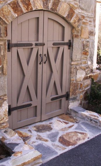Wooden arched double doors with an X design, tan with black hardware, set in a stone archway, stone path.