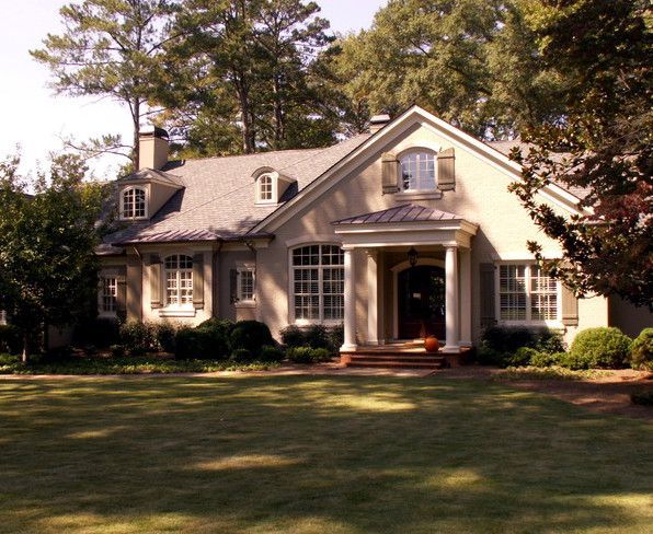 Tan house with white trim, green lawn, and lush landscaping.