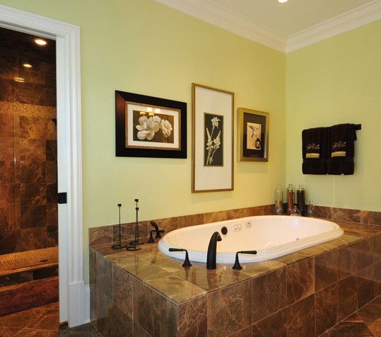 A luxurious bathroom with a jacuzzi tub, surrounded by brown marble. Green walls, framed art, and a shower entrance.