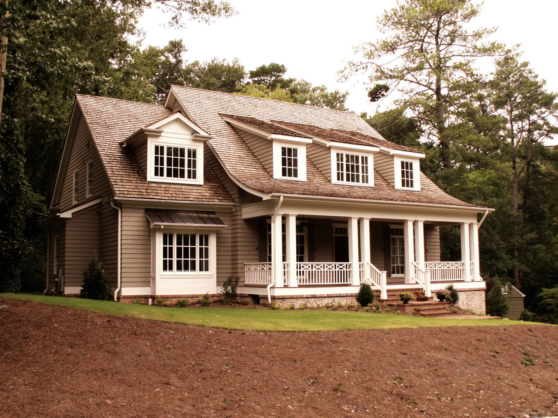 Tan Craftsman-style house with a porch and dormers surrounded by trees.