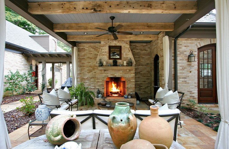 Outdoor patio with stone fireplace, rustic beams, furniture, and decorative vases.