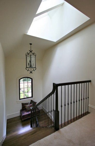 Staircase with black railing and chandelier, leading to a window seat under a skylight.