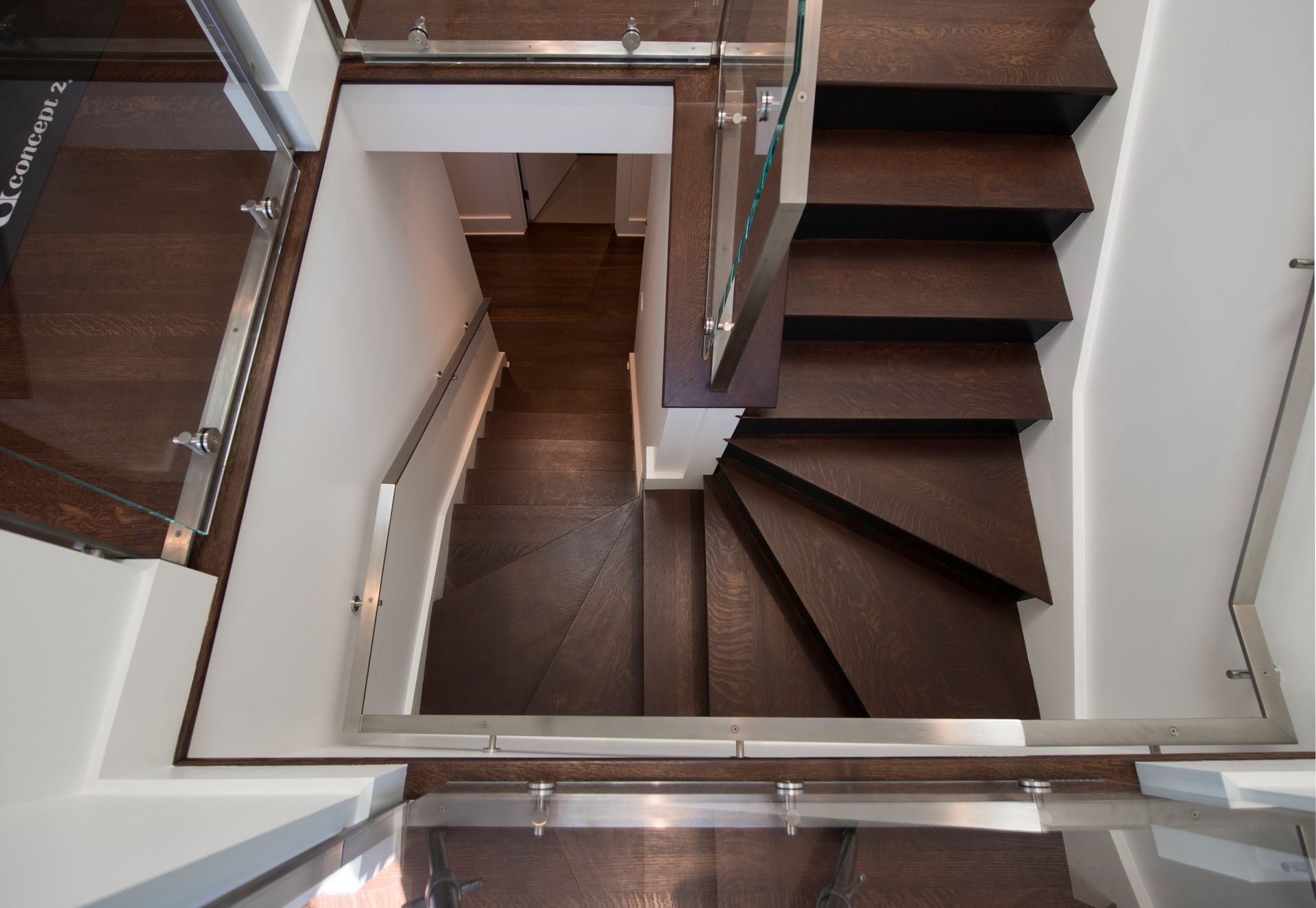 Dark wooden staircase with glass and metal railing, viewed from above.