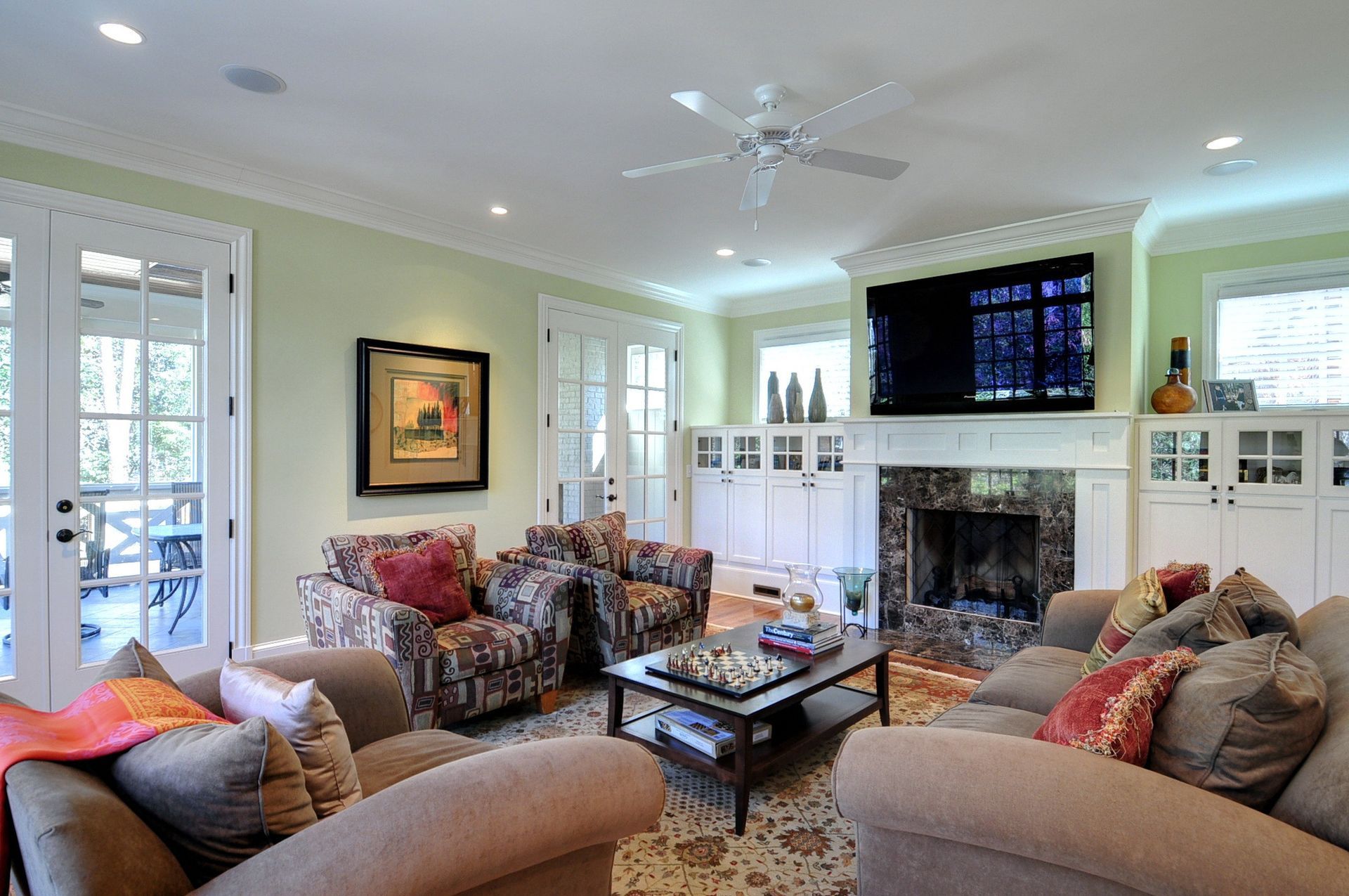 Living room with beige sofas, patterned armchairs, fireplace, TV, and French doors to a deck.